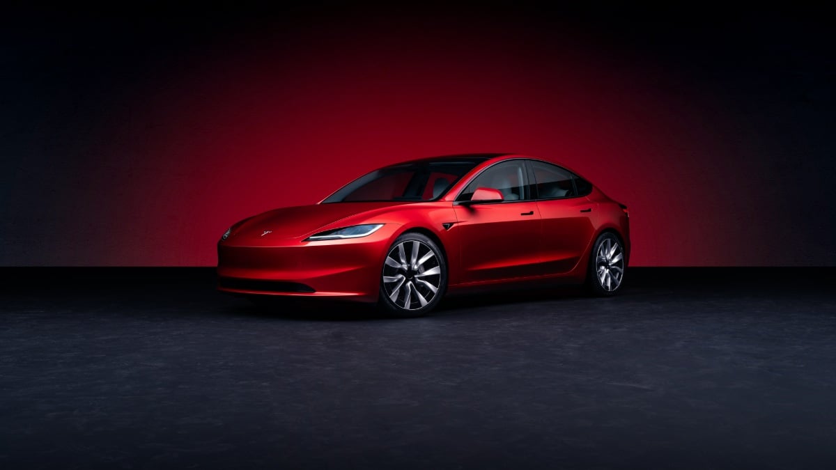 Red 2025 Tesla Model 3 electric sedan photographed from a front three-quarter angle in a studio setting